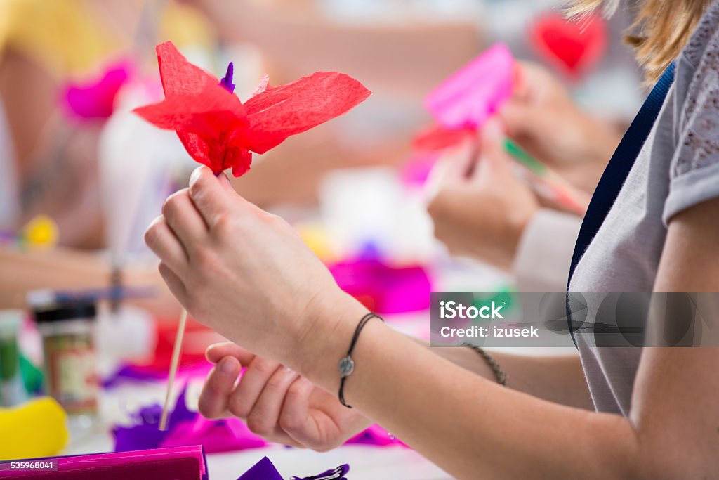 Women making paper flowers Group of women working on workshop, making coloful paper flowers. Close up of hand holding flower. Unrecognizable person. 2015 Stock Photo