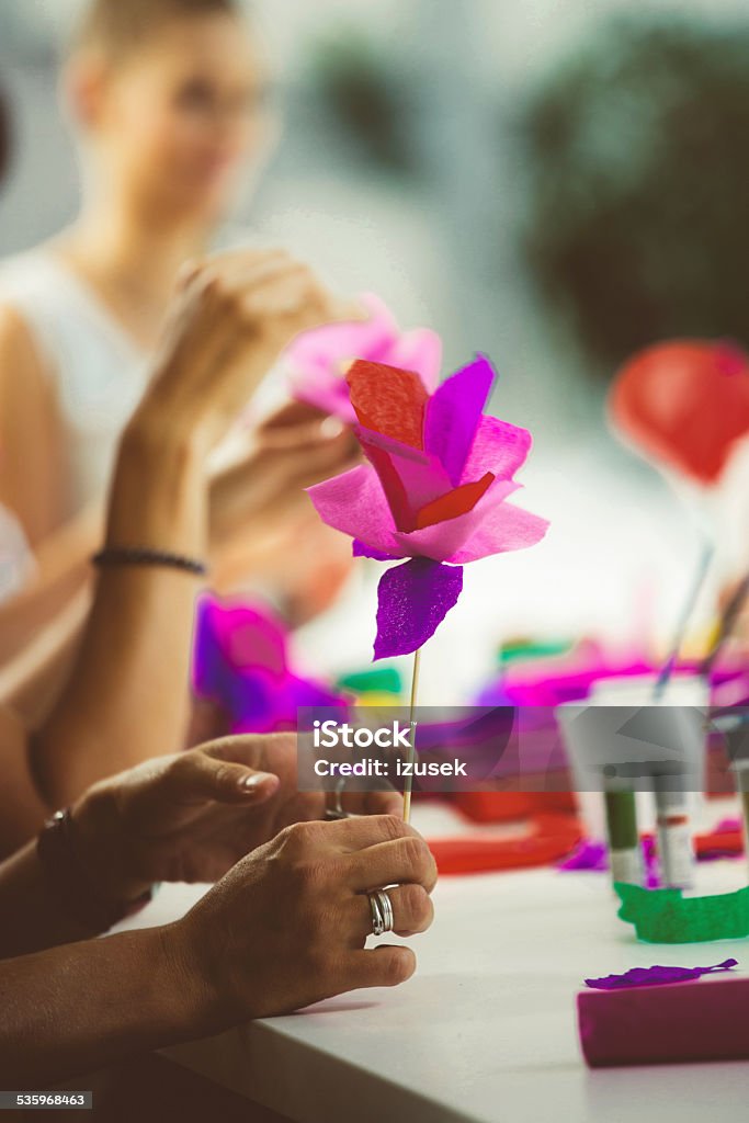 Women making paper flowers Group of women working on workshop, making coloful paper flowers. Close up of hands holding flower. Unrecognizable person. 2015 Stock Photo