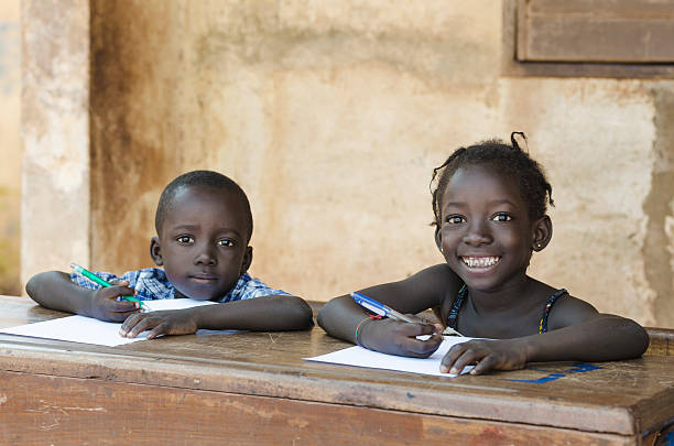 Cute Little Children Learning with Pens Paper in Mali, Africa Couple of African Ethnicity Children laughing at smiling whilst sitting at school as an education symbol for Africa (picture taken in Bamako, Mali). Blurred background. School environment. mali stock pictures, royalty-free photos & images