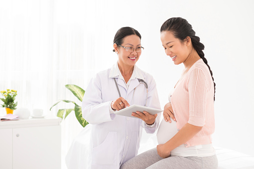 Vietnamese doctor using digital tablet at meeting with pregnant woman