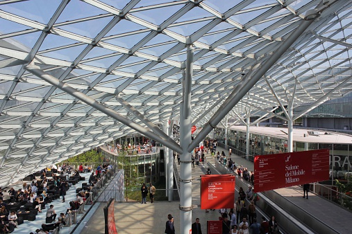 Milan, Italy - April 9, 2014: Milan Trade fair pavillion during the Salone del Mobile 2014, view from the top of the main promenade with people walking and the architectural transparent glass and steel roof