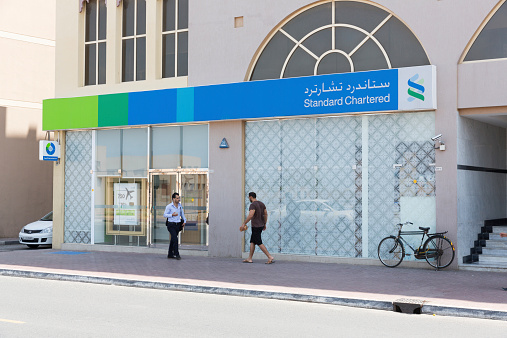 Dubai, United Arab Emirates - March 27, 2014: People walk past the Standard Chartered Bank in Dubai, United Arab Emirates. It is a British multinational banking and financial services company.