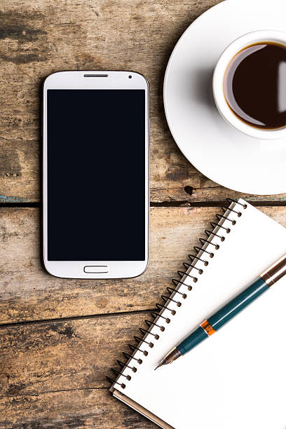 Smart phone with notebook and cup of strong coffee Smart phone with notebook and cup of strong coffee on wooden background. Cellphone with writing set with espresso whites only drinking fountain stock pictures, royalty-free photos & images