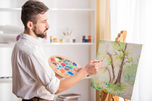 Stylish Israeli abstract artist stands in from of his paintings with arms crossed staring into the camera