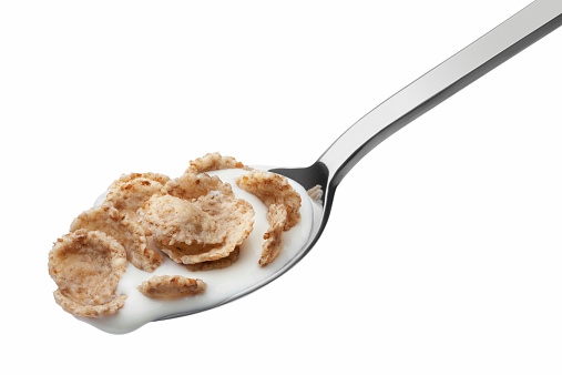 Corn flakes and yogurt in a metal spoon isolated white background