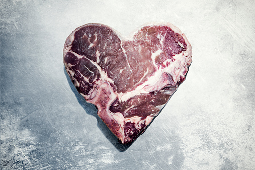 A raw T-bone steak in the shape of a heart on a worn stainless steel table.  Concept for Valentines day, heart health, love, meat consumption and safety, etc.  Horizontal image with copy space.