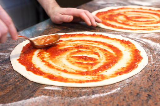 Tomato sauce being spread on pizza base.