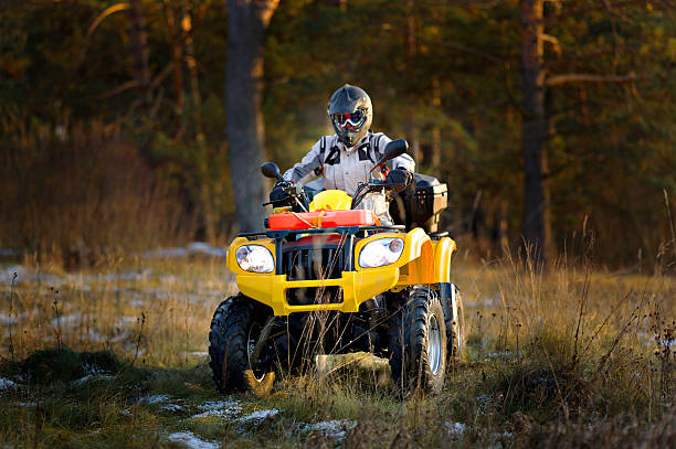 Man driving quad bike Horizontal portrait of a man in helmet and safety goggles looking into the camera while sitting on all-terrain vehicle against snowy late autumn landscape. quadbike photos stock pictures, royalty-free photos & images