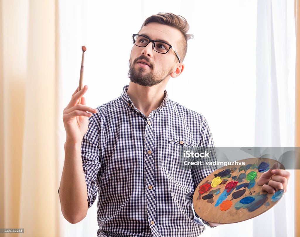 Artist Portrait of a young male artist is holding a brush and mix color oil painting on palette.Young male artist is drawing on an easel and holding palette in hand. 2015 Stock Photo