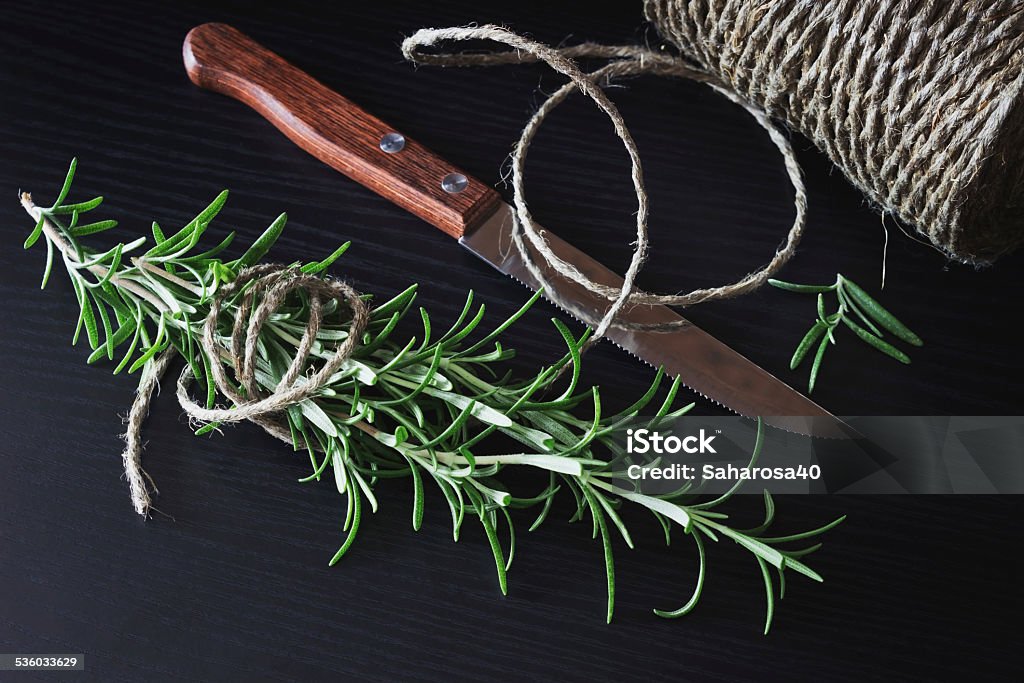 rosemary twig of fresh rosemary, a kitchen knife and a skein of of flax rope on black wooden table.  food concept. healthy food from garden 2015 Stock Photo