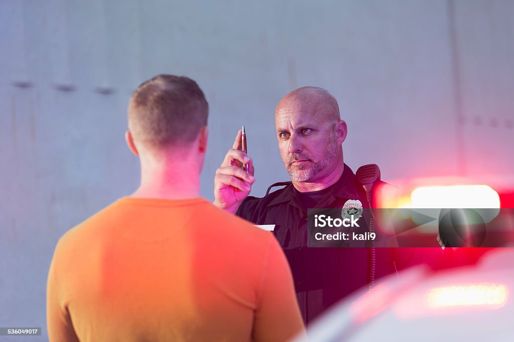 Policeman performing sobriety test on driver Police officer giving sobriety test to young man to see if he is driving under the influence of drugs or alcohol.  Police cruiser is out of focus in the foreground. Drunk Driving Stock Photo