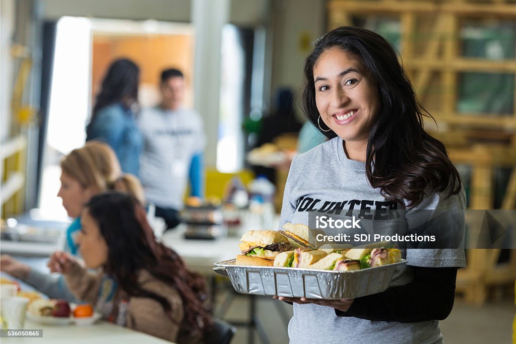 Friendly Hispanic woman serving food at neighborhood charity soup kitchen Soup Kitchen Stock Photo