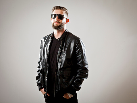 Studio photograph of young bearded man wearing leather jacket and sunglasses. Copy space.