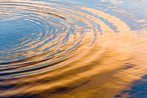 Water ripples on Lake Windermere at sunset, with cloud and sky reflections in gold and blue.