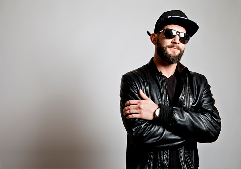 Studio photograph of young bearded man wearing leather jacket,hat and sunglasses. Copy space.