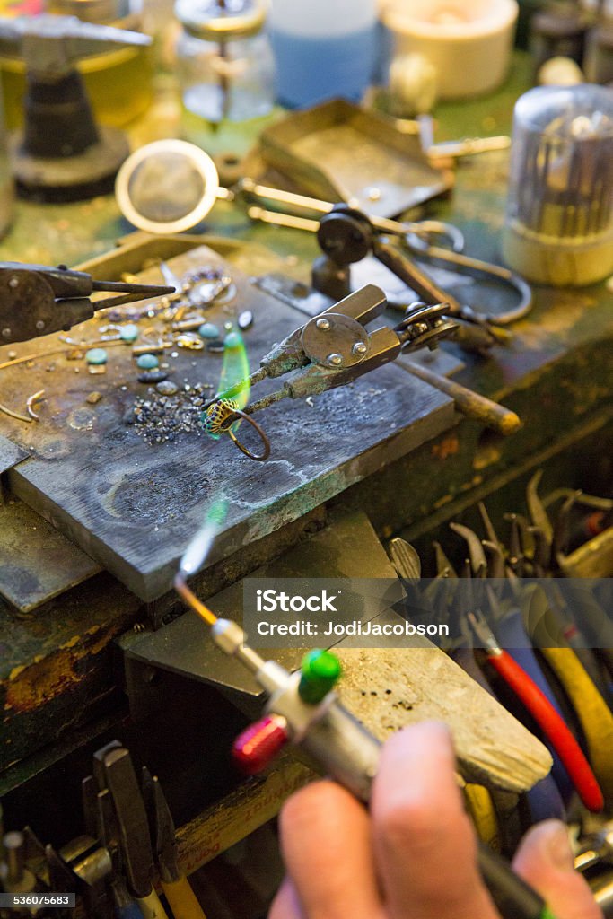 Jeweler heating piece of gold at jeweler's workbench A piece of gold is being heated by a jeweler before being shaped at a jeweler's workbench.  Shot with Canon 5D Mark 3.  rr 2015 Stock Photo