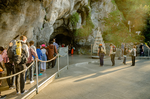 Lourdes, France - April 16, 2014: Grotto is a Catholic shrine to Our Lady in Lourdes. Pilgrims can process through the grotto and touch the rocks under the statue. Rows of benches allow visitors to sit and pray or contemplate.