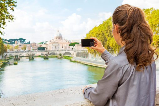 Young woman taking photo while on bridge ponte umberto I with view on basilica di san pietro
