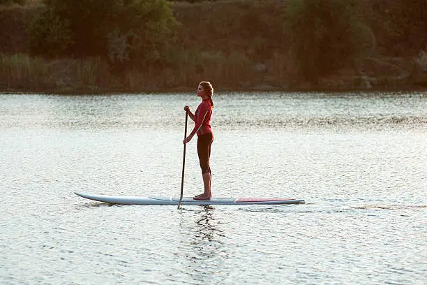 confident woman standing with a paddle on the surfboard