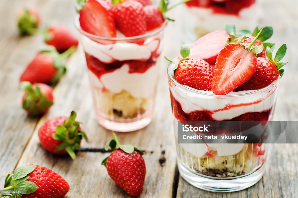 layered dessert with strawberries, biscuit cake and cream cheese layered dessert with strawberries, biscuit cake and cream cheese on a dark wood background. tinting. selective focus 2015 Stock Photo