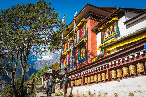 Namche Bazaar, Nepal - 20th October 2011: Young Nepalese men walking past the colourful Buddhist monastery and traditional prayer wheels in Namche Bazaar, Sherpa trading post and gateway to the Mt. Everest region deep in the Himalaya mountains of the Sagarmatha National Park, a UNESCO World Heritage Site.