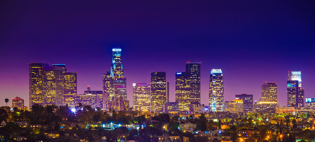 The panoramic skyline cityscape of Los Angeles downtown skyscrapers at nighttime twilight. Distant shot with atmospheric distortion.