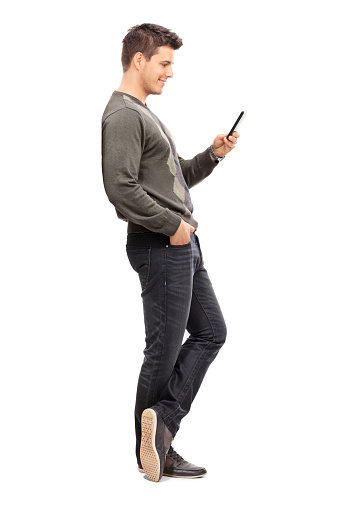 Full length portrait of a young man texting on his cell phone isolated on white background