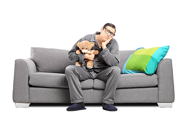 Sad man in pajamas holding a teddy bear Sad man in pajamas holding a teddy bear seated on a sofa isolated on white background man with teddy bear stock pictures, royalty-free photos & images