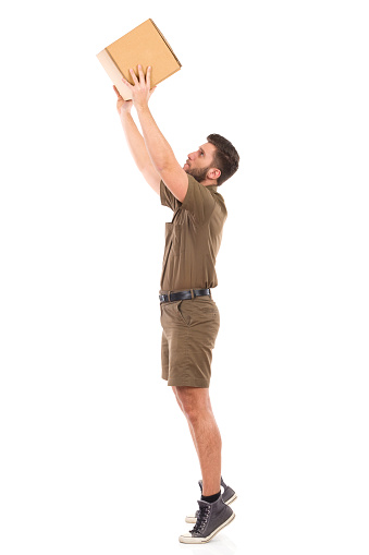 Delivery man in khaki uniform picking up a carton box. Full length studio shot isolated on white.