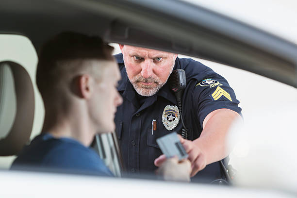 Police officer making a traffic stop A serious police officer reaching for the ID card of a young driver he pulled over.  The officer is standing outside the car, looking through the driver's window.  The young man sitting in the car is out of focus. driving under the influence stock pictures, royalty-free photos & images