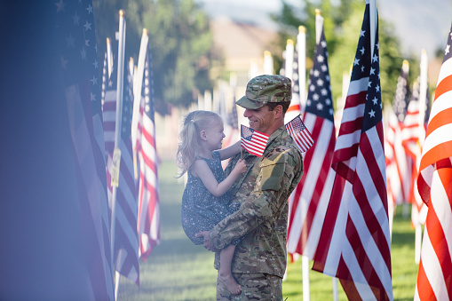 An American soldier standing in a field of American flags holding his preschool daughter.