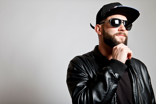 Studio photograph of young bearded man wearing leather jacket,hat and sunglasses. Copy space.