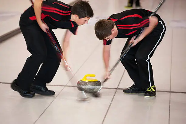Two boys sweeping the rock/stone in curling.  Motion blurred image