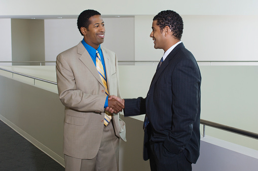 Two business men shaking hands in office hallway