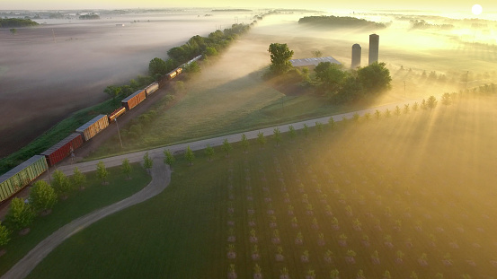 Railroad train rolls across breathtakingly beautiful, foggy landscape at sunrise.