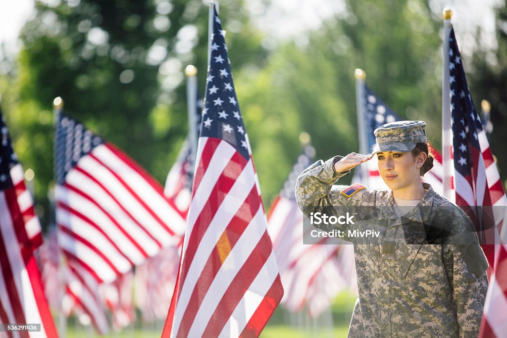 Femme soldat américain saluant devant drapeaux américains - Photo de Faire le salut militaire libre de droits