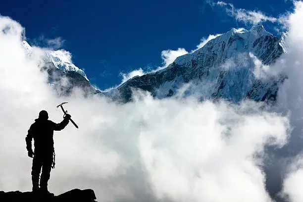 Silhouette of man with ice axe in hand and mountains with clouds - Mount Thamserku and Mount Kangtega - Nepal
