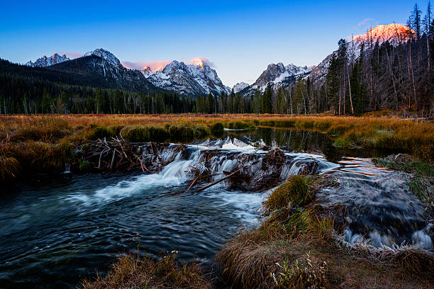 Beautiful snow covered Sawtooth mountain range reflecting in calm waters of a mountain lake or a beaver dam on a fine autumn morning in Stanley, Idaho, USA