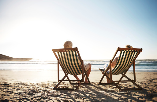 Rearview shot of a senior couple relaxing in beach chairs while looking at the view over the water