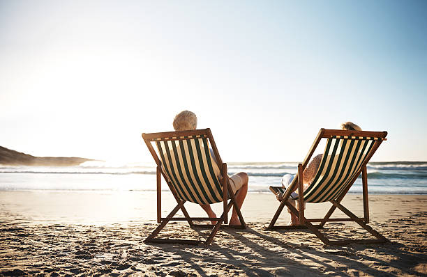The perfect day Rearview shot of a senior couple relaxing in beach chairs while looking at the view over the water deck chair stock pictures, royalty-free photos & images