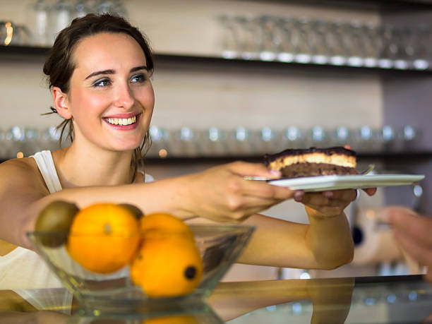 Offering cake at the bar counter Portrait of young beautiful woman working at the bar counter of restaurant in Portoroz, Slovenia. sunken cake stock pictures, royalty-free photos & images