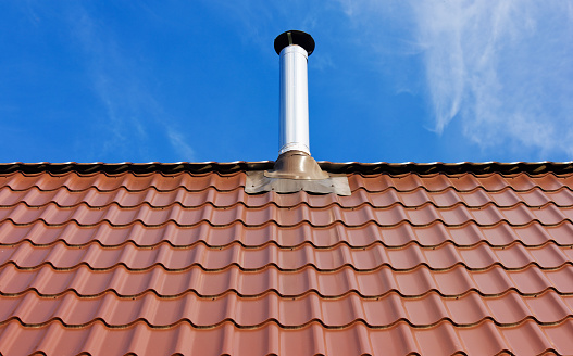Red tile roof with a tin chimney under the sun on a blue sky background with white clouds