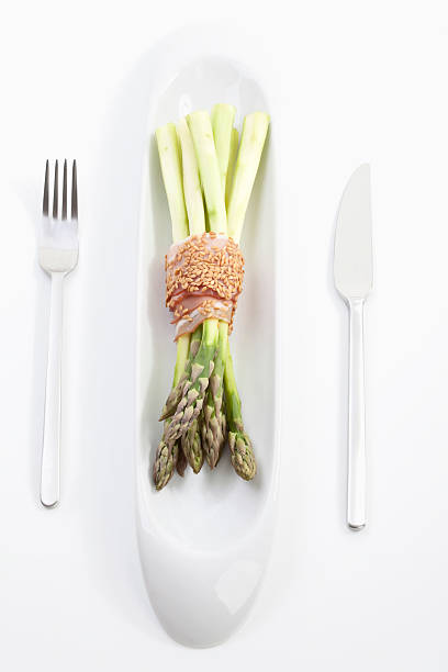 Asparagus with ham and sesame in glass on white background