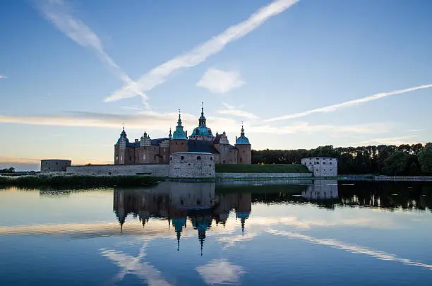 The swedish medieval Kalmar Castle at evening with steam lines in the sky.