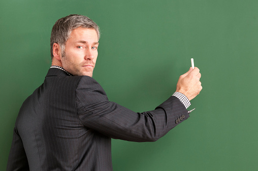 attractive serious teacher with grey hair writing at blackboard 