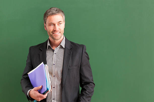 istock smiling teacher with grey hair at blackboard 536403245
