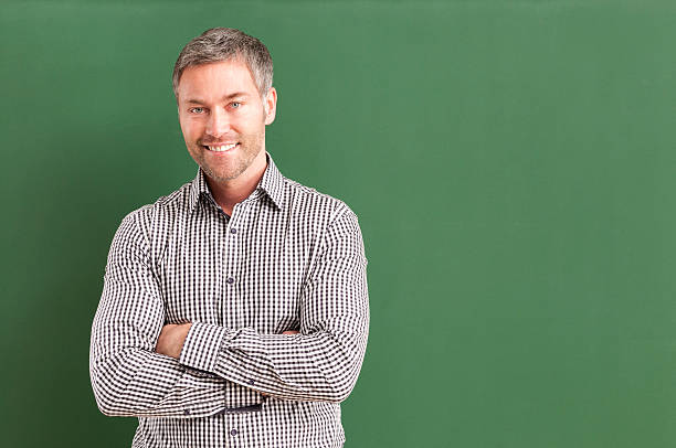istock smiling teacher with arms crossed standing at blackboard 536403251