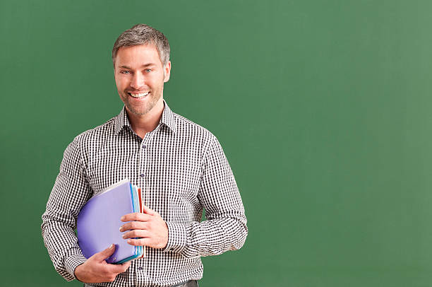 istock smiling teacher with grey hair at blackboard 536403253