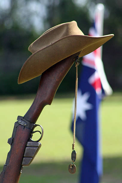 ANZAC Day Army Rifle, Slouch hat, Dogtags and Australian Flag Portrait shot (with room for copy) of an upturned, vintage Australian Army 303 rifle, a soldier's dogtags, slouch hat with an Australian Flag flying in the background during an ANZAC Day memorial service. larrikin stock pictures, royalty-free photos & images
