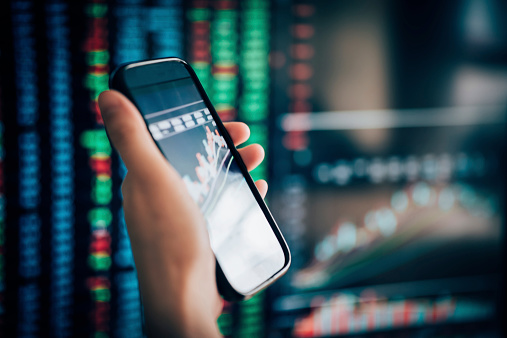 cell phone on hand with stock market data background
